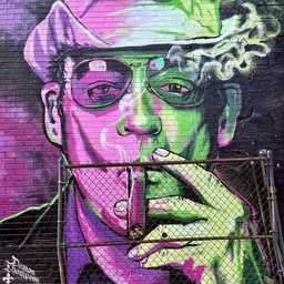 A surreal urban mural portrays a man wearing a hat, cigarette smoke drifting into the air as neon pink and green light washes across his face. The vibrant colors and oversized portrait dominate the dark wall behind an aging chain-link fence.