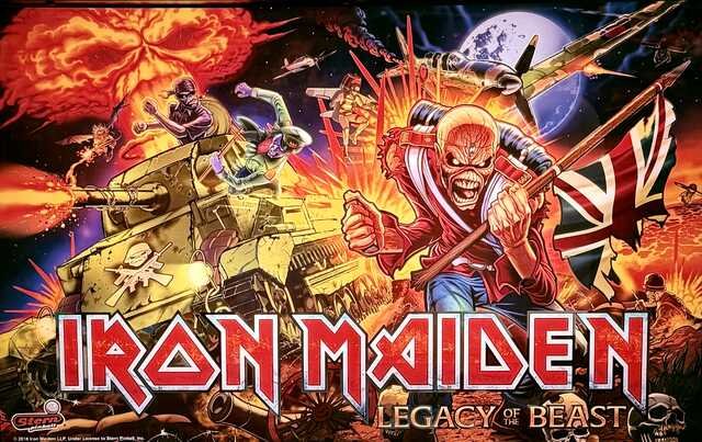 Colorful backglass artwork from the Iron Maiden: Legacy of the Beast pinball machine. Iron Maiden's skeletal mascot, Eddie, charges forward carrying a tattered Union Jack as explosions erupt behind him. A tank, fighter planes, and soldiers battle across a fiery war-torn landscape beneath a full moon.